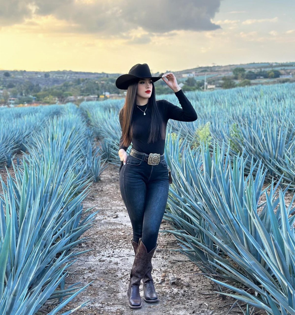 10 Cute Country Outfits with Denim, Boots, and Fringe 5 Woman in cowboy hat and boots posing in a blue agave field