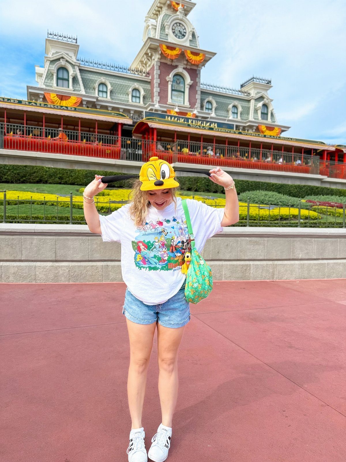 10 Cute Disney Outfits to Wear at the Parks in 2026 6 Woman wearing a white graphic tee, denim shorts, and yellow Pluto ears at Disney.