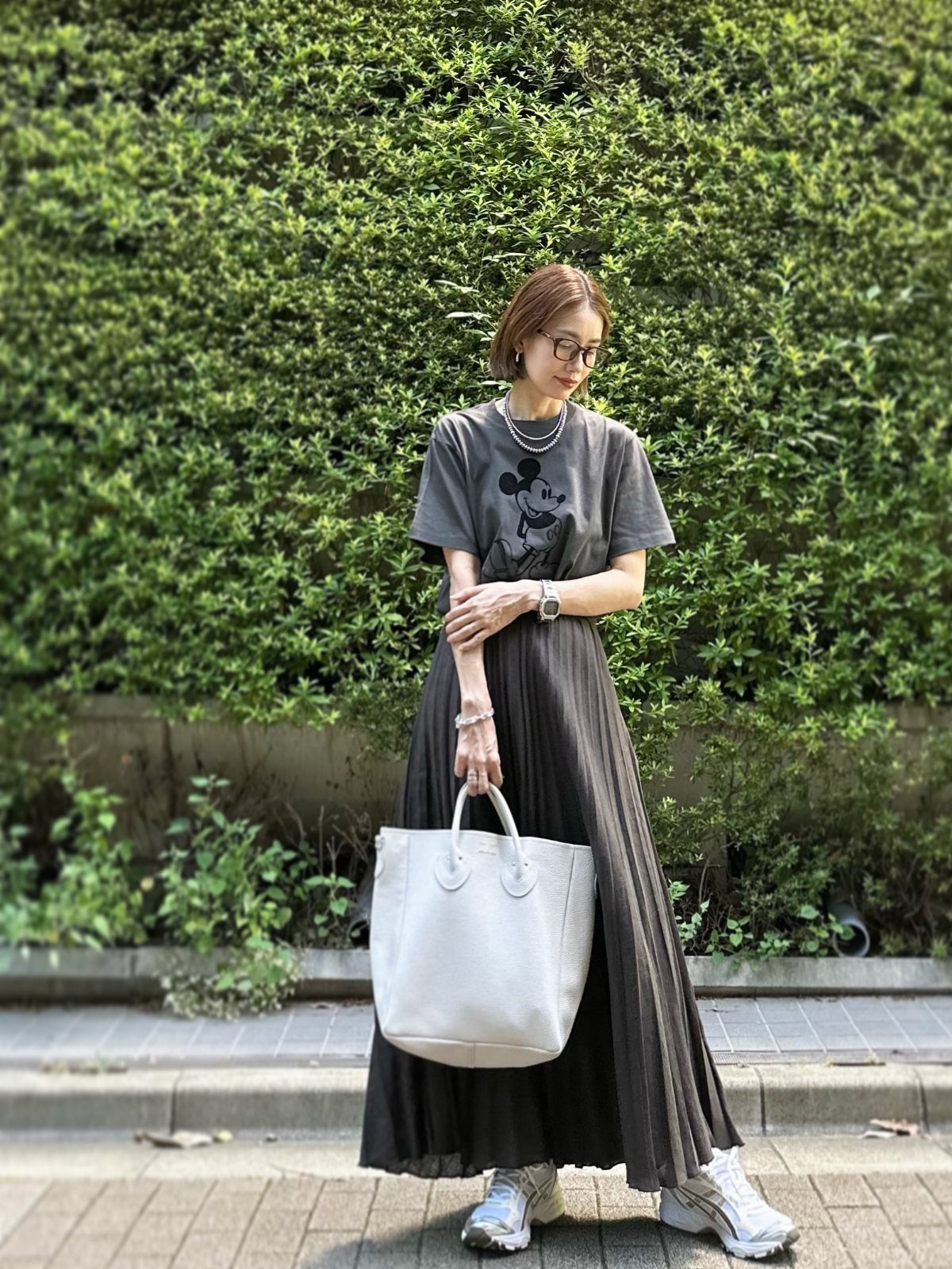 10 Cute Disney Outfits to Wear at the Parks in 2026 8 Woman wearing a grey Mickey Mouse graphic tee and long pleated dark grey skirt.