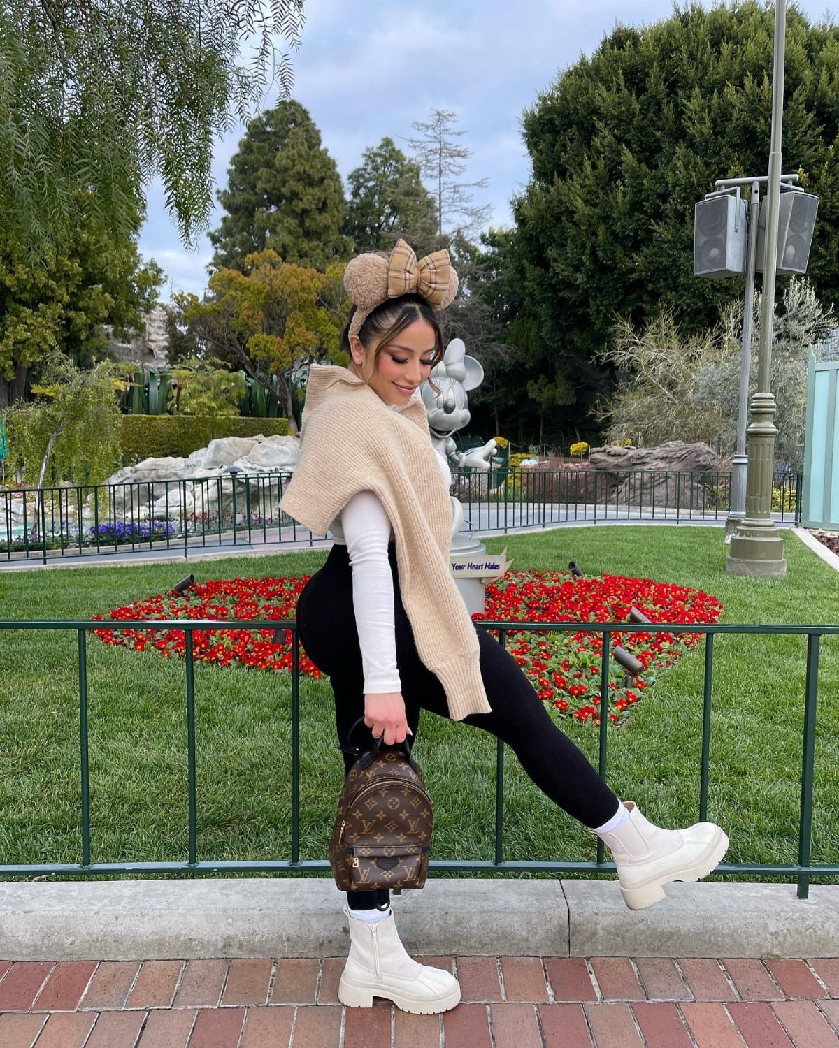 10 Cute Disney Outfits to Wear at the Parks in 2026 2 Woman wearing a tan bow ear headband and white boots at a theme park.