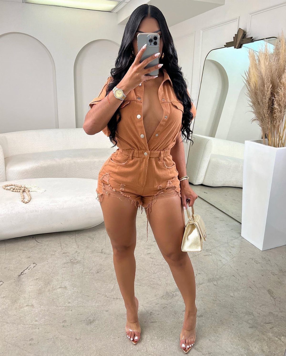 12 Cute Summer Outfits to Keep You Cool and Stylish 3 Woman wearing a brown short-sleeved romper and clear high-heeled sandals in a white room.