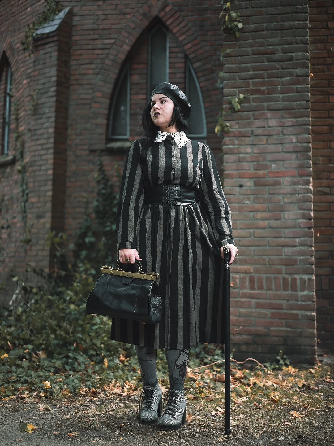 Dark Academia Outfits Female: 12 Ideas for Timeless Style 5 Woman in striped dress and black leather belt posing by a brick wall.