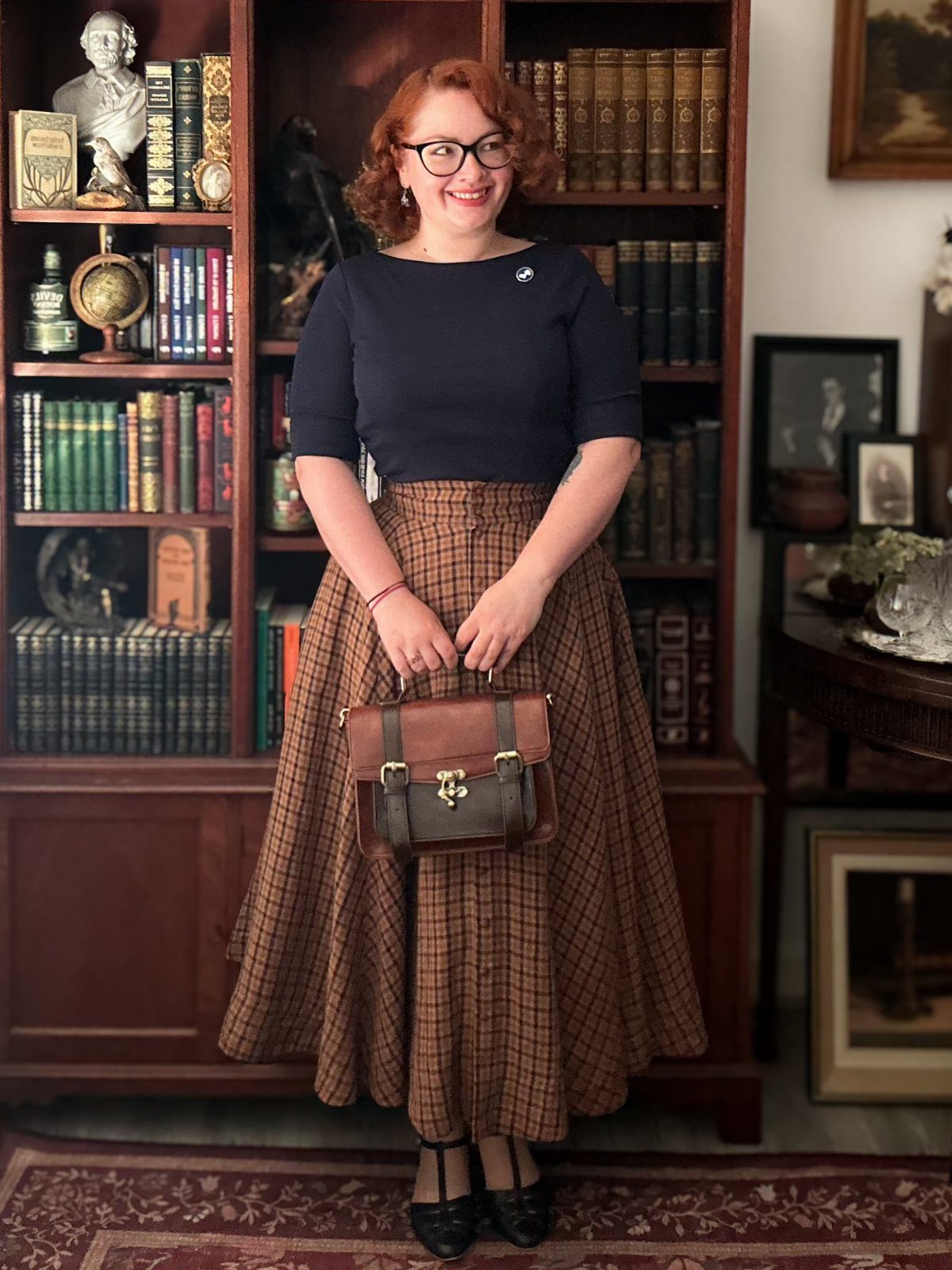 Dark Academia Outfits Female: 12 Ideas for Timeless Style 1 Woman in navy top and brown plaid skirt holding a leather satchel bag.