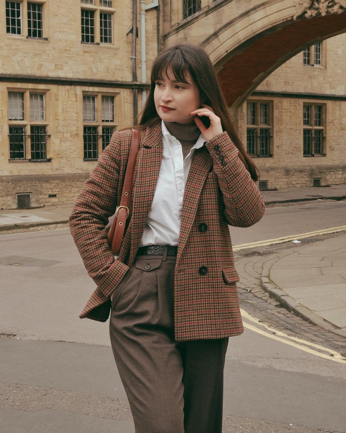 Dark Academia Outfits Female: 12 Ideas for Timeless Style 3 Woman wearing a brown plaid blazer and turtleneck in front of stone architecture.