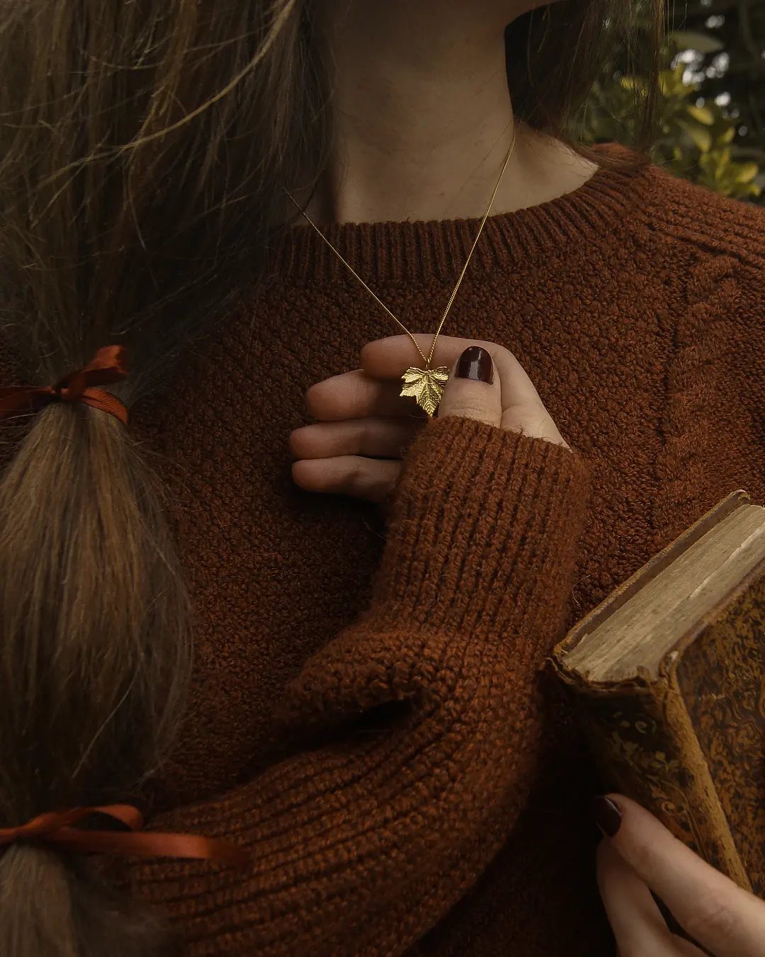 Dark Cottagecore Outfits: 8 Ideas from Dresses to Footwear 4 Gold leaf pendant necklace and brown hair ribbons worn with a knit sweater.