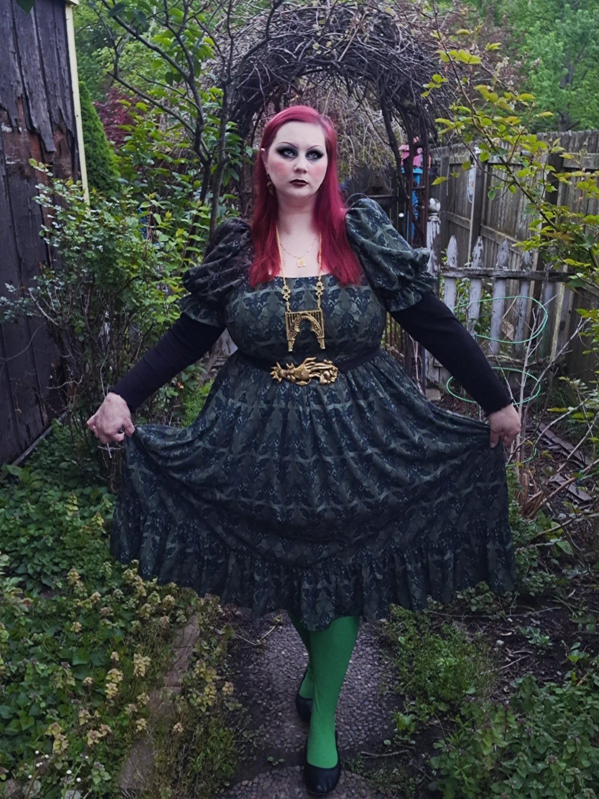 Dark Cottagecore Outfits: 8 Ideas from Dresses to Footwear 6 Person with red hair in a dark green cottagecore dress standing in a garden.