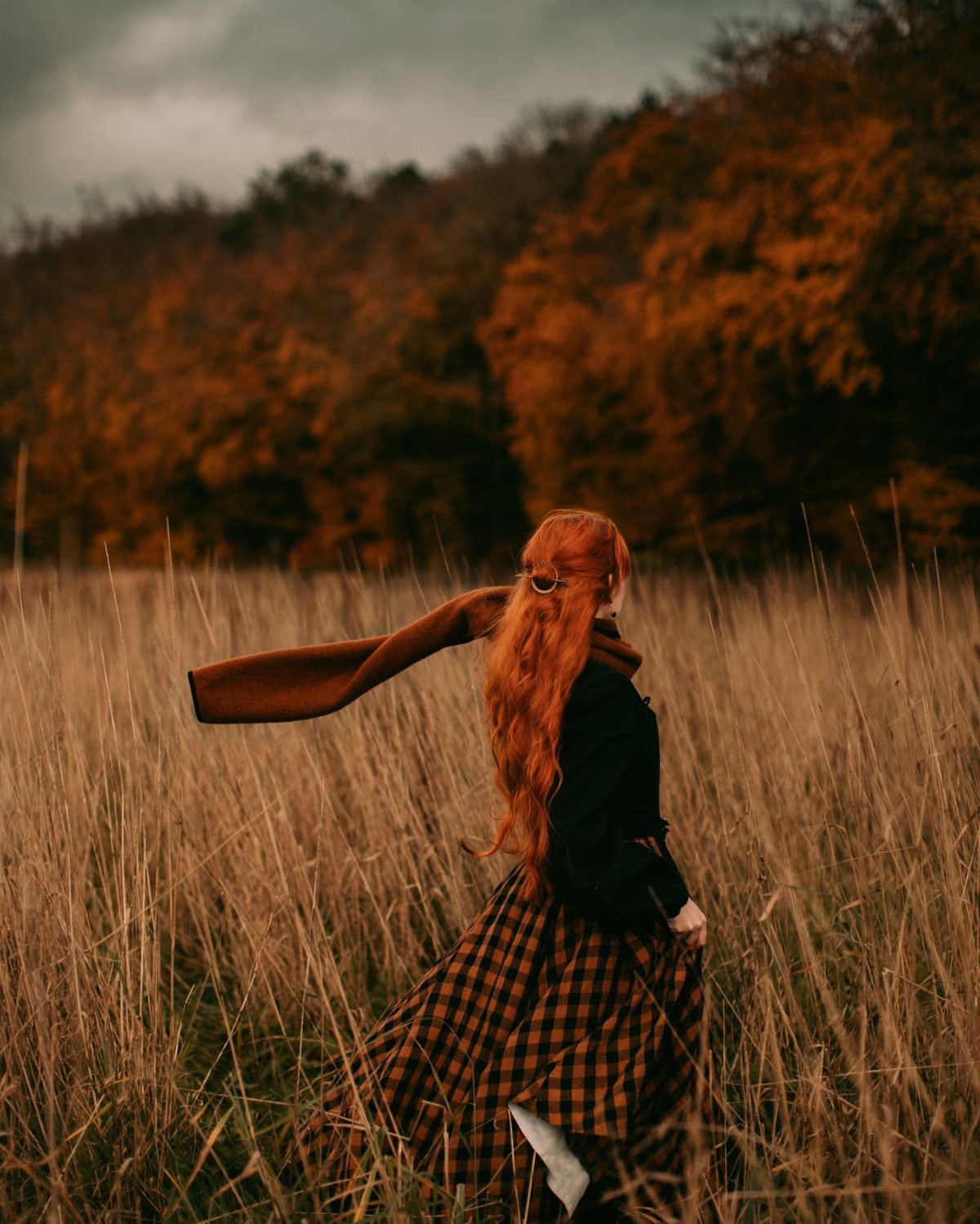 Dark Cottagecore Outfits: 8 Ideas from Dresses to Footwear 5 Red-haired person in a plaid skirt and brown scarf in an autumn field.