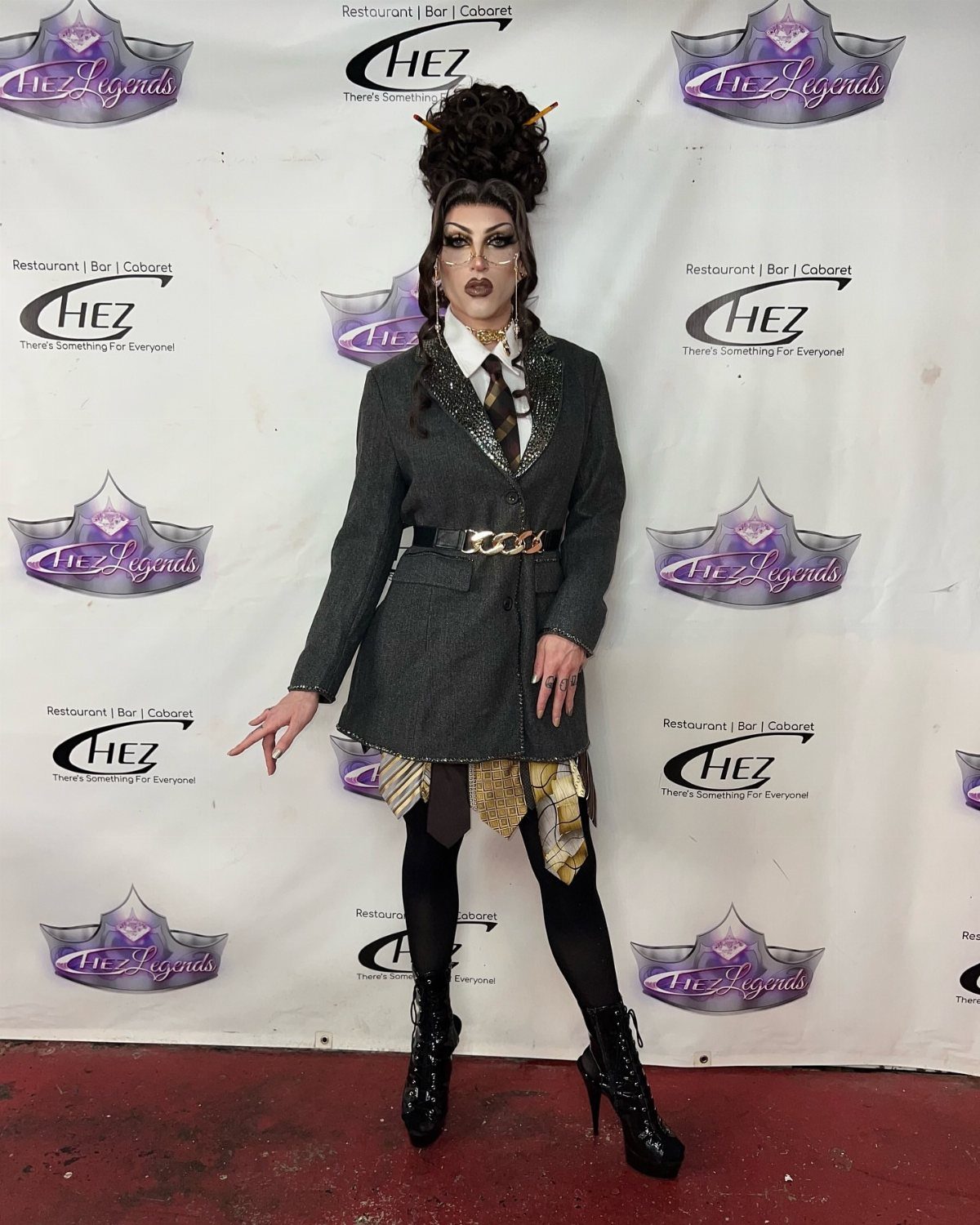 Drag Queen Outfits: 8 Bold Ideas for Your Next Performance 5 Drag queen wearing a grey blazer, patterned layered skirt, and high black boots.