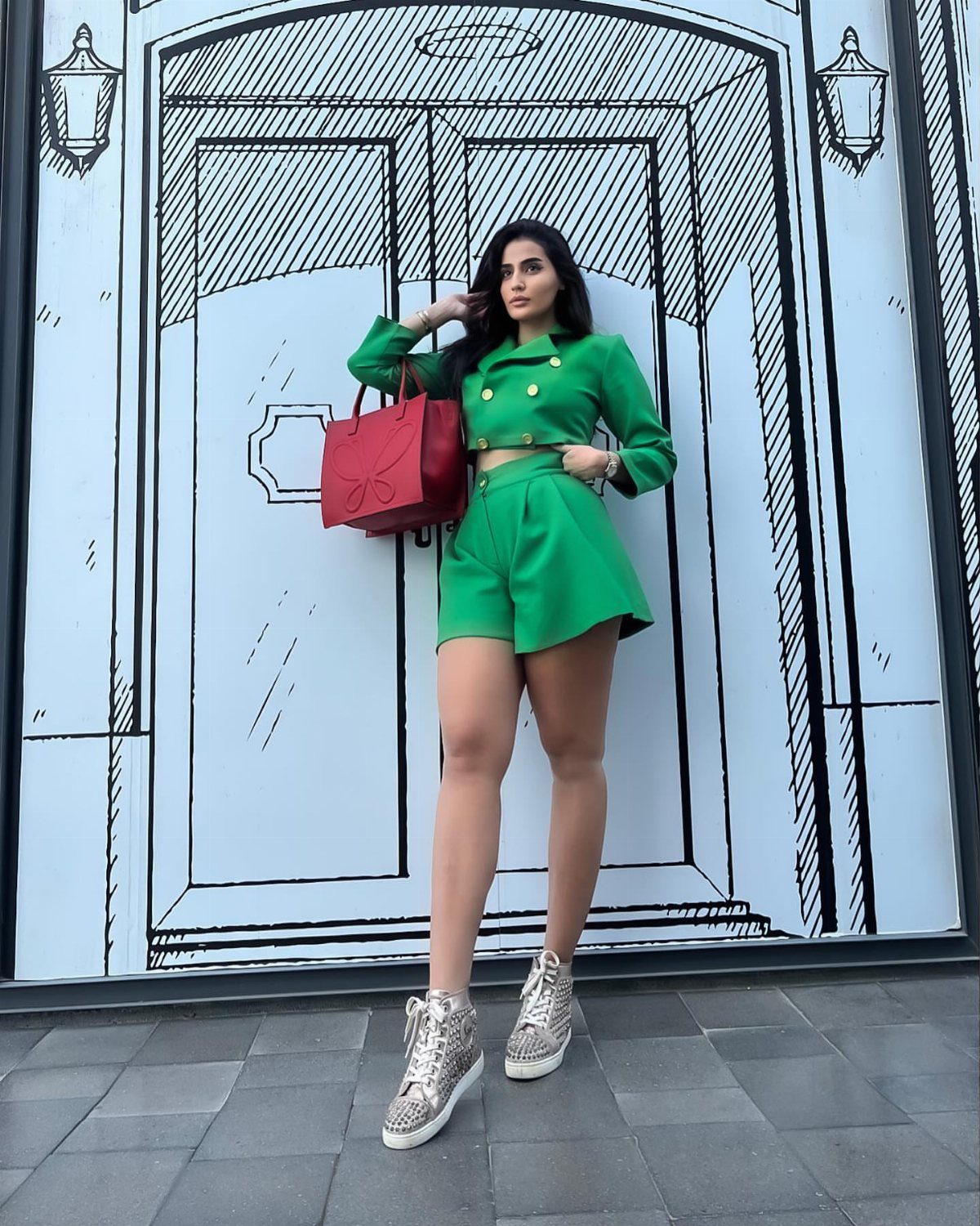 Dua Lipa Concert Outfits: 7 Show-Stopping Looks to Try 6 Woman in green cropped blazer and shorts posing before a sketched door background.