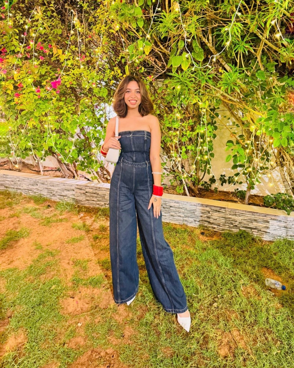 Dua Lipa Concert Outfits: 7 Show-Stopping Looks to Try 7 Woman in a strapless dark blue denim jumpsuit posing in a garden.