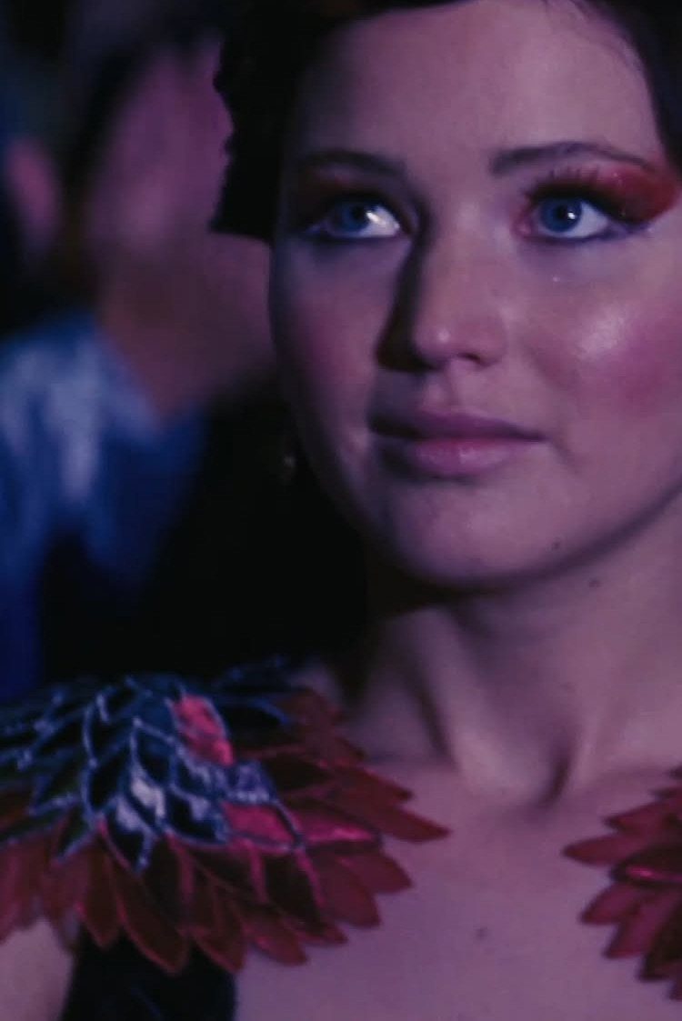 Effie Trinket Outfits: 10 Iconic Looks to Recreate 9 Woman with dramatic red eyeshadow and red petal-like shoulder details on her outfit.