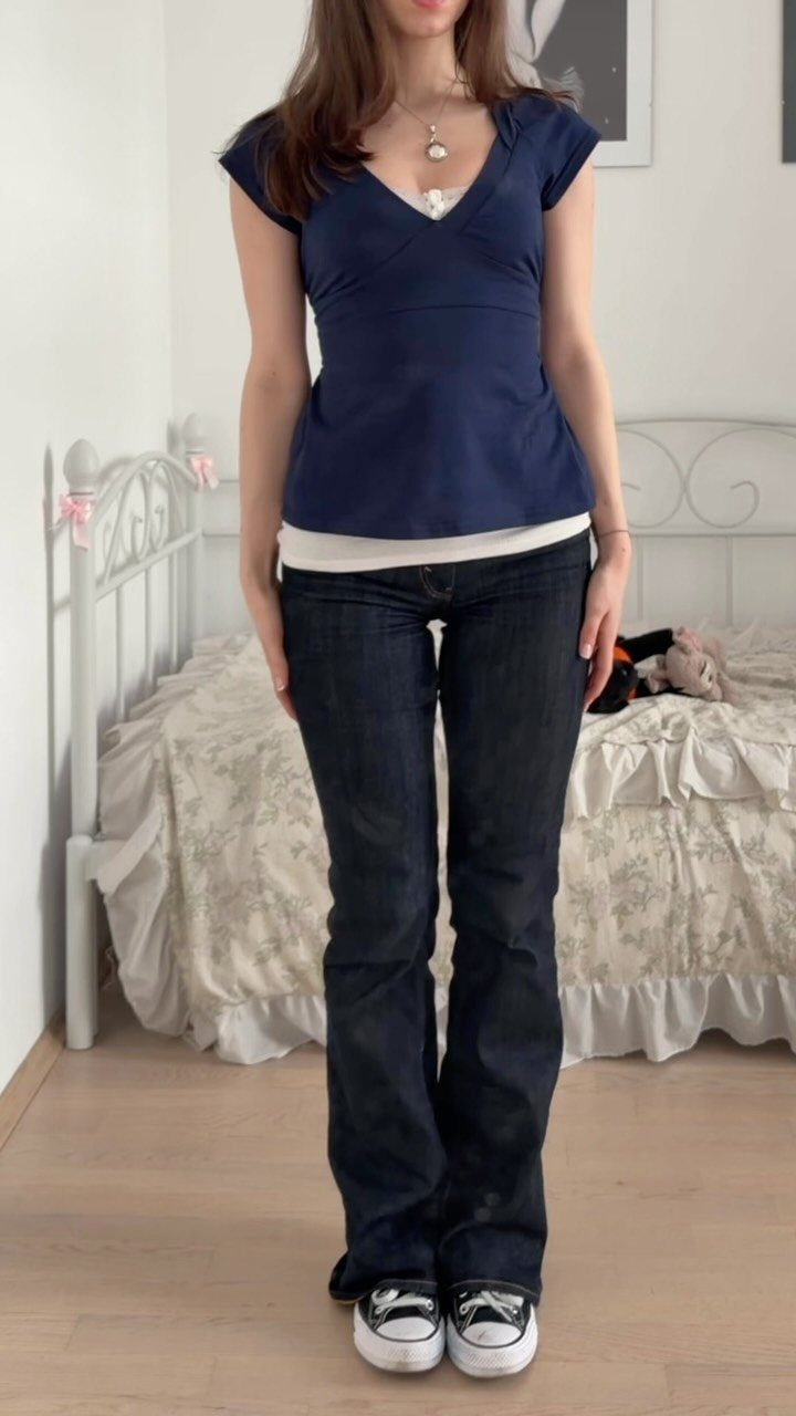 14 Elena Gilbert Outfits: Her Best Looks from the Show 11 Person wearing a blue V-neck top and flared jeans in a bedroom setting.