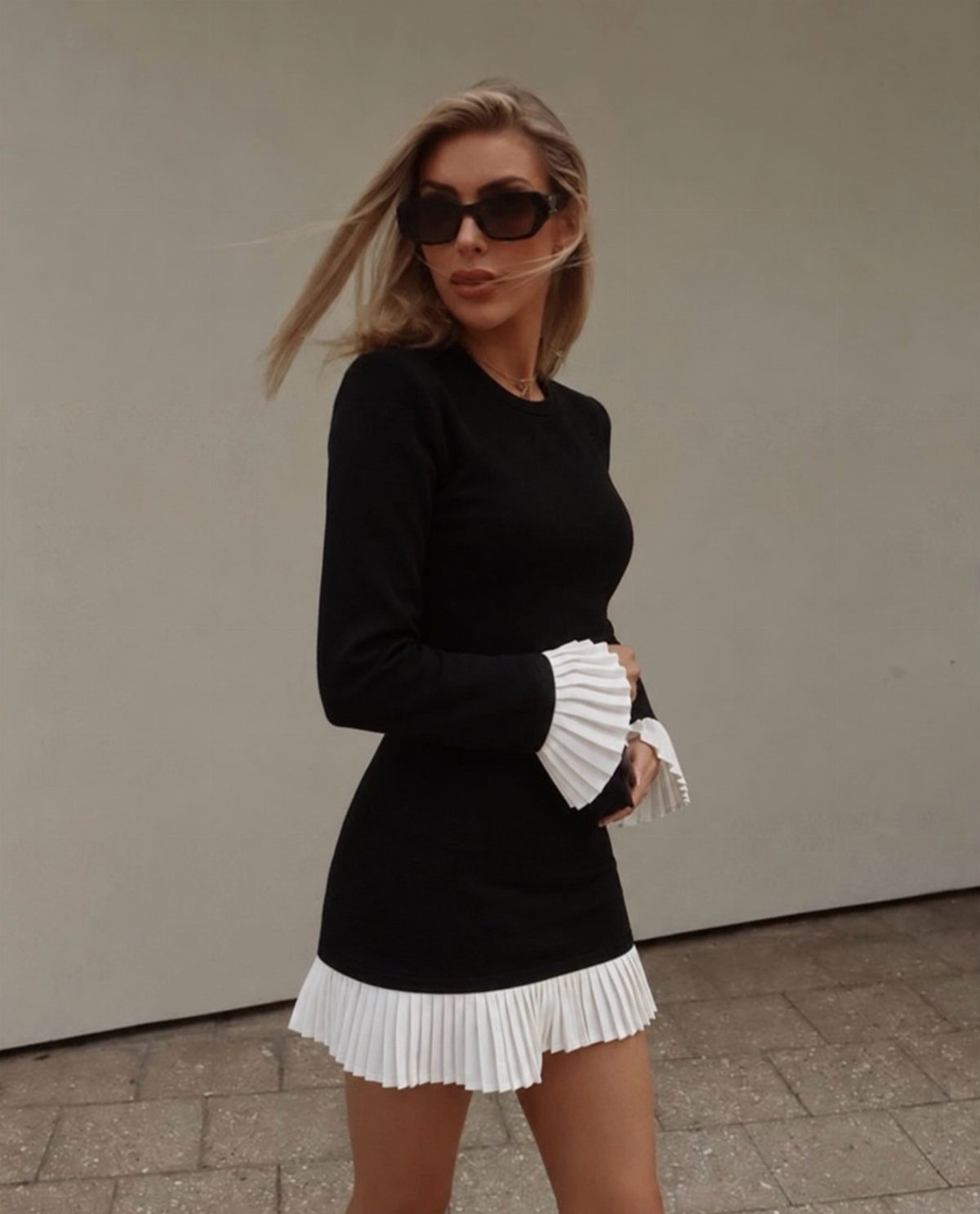 10 Elle Woods Outfits That Defined a Generation of Style 2 Woman wearing a black long-sleeved dress with white pleated ruffles on cuffs and hem.
