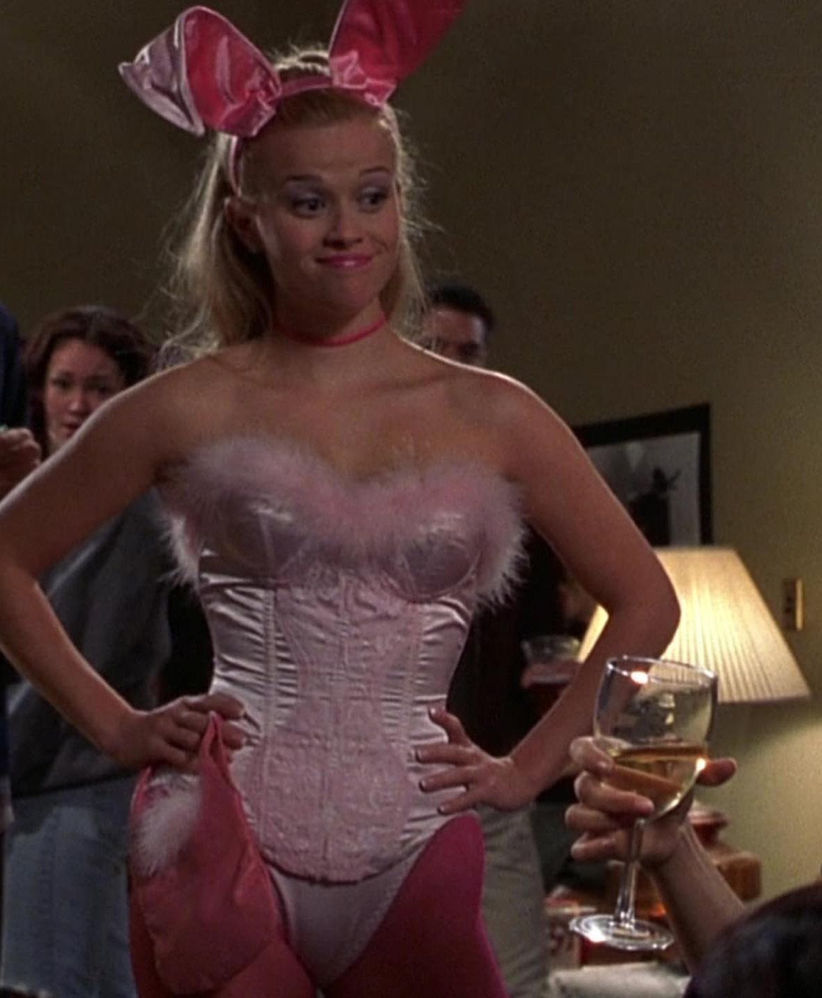 10 Elle Woods Outfits That Defined a Generation of Style 6 Woman wearing a pink satin corset and bunny ears posing indoors.