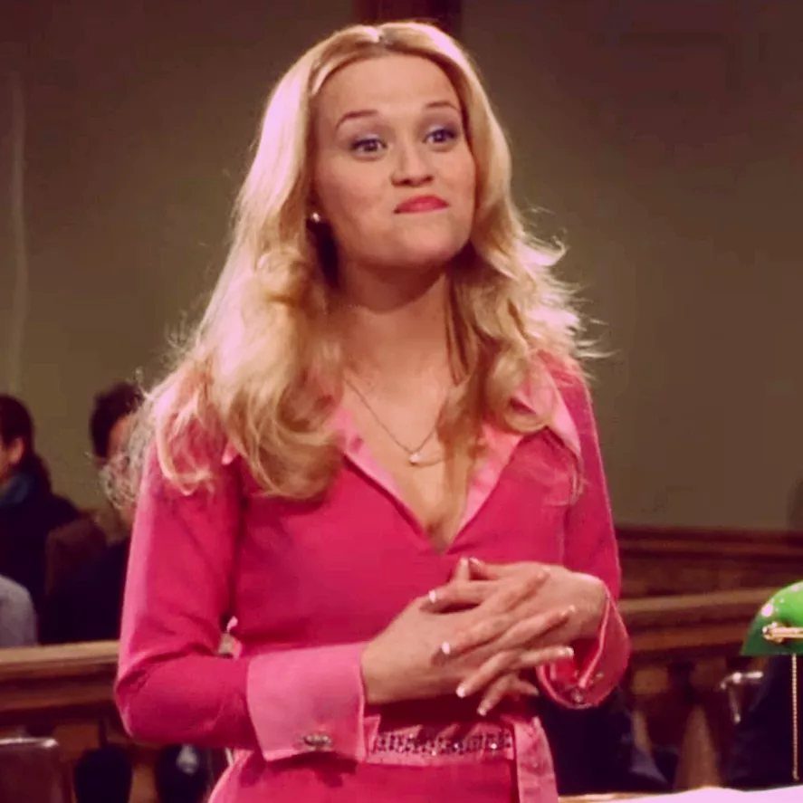 10 Elle Woods Outfits That Defined a Generation of Style 5 Blonde woman in a bright pink tailored blazer standing in a courtroom.