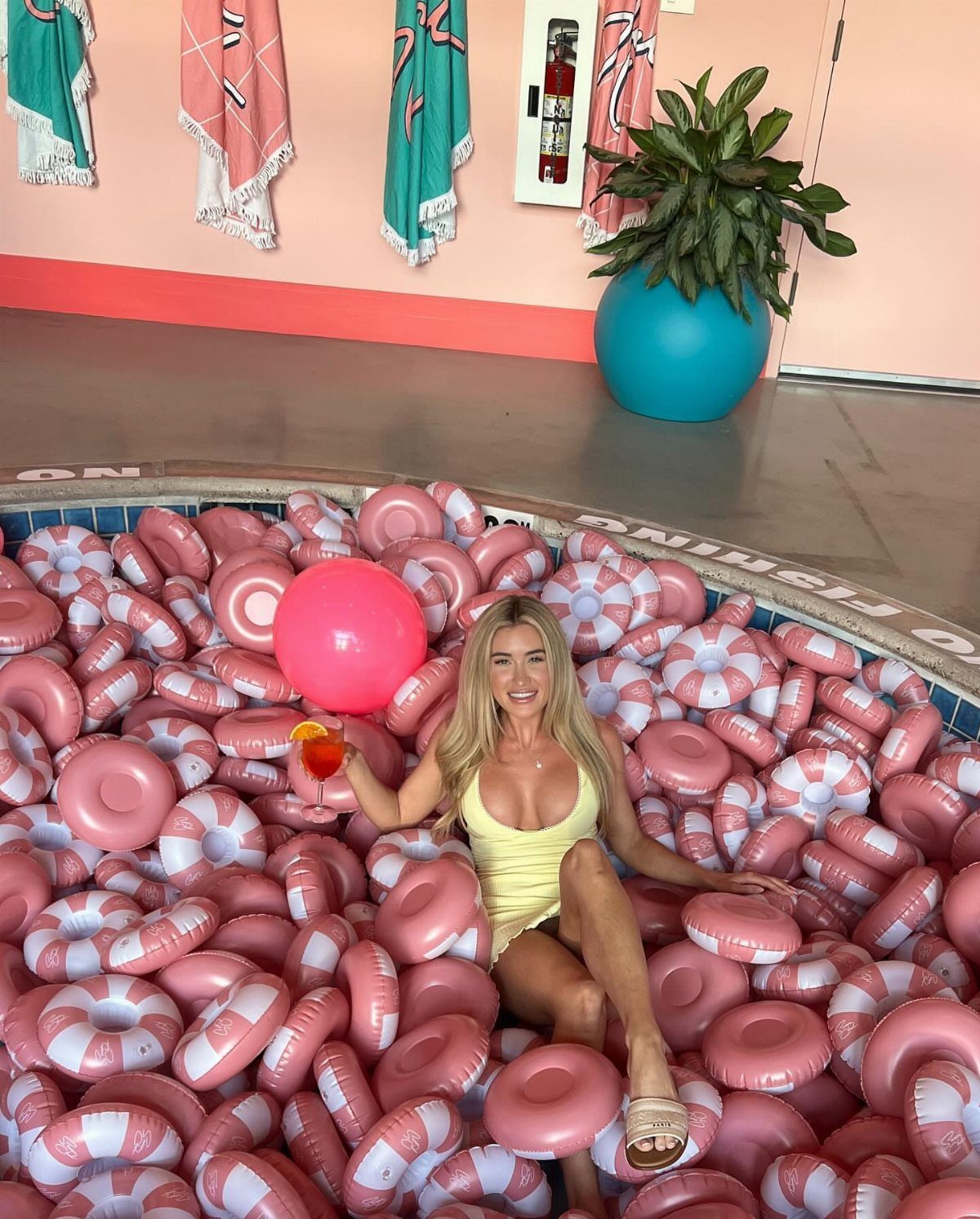 10 Elle Woods Outfits That Defined a Generation of Style 9 Blonde woman in yellow dress sitting among pink and white inflatable rings.
