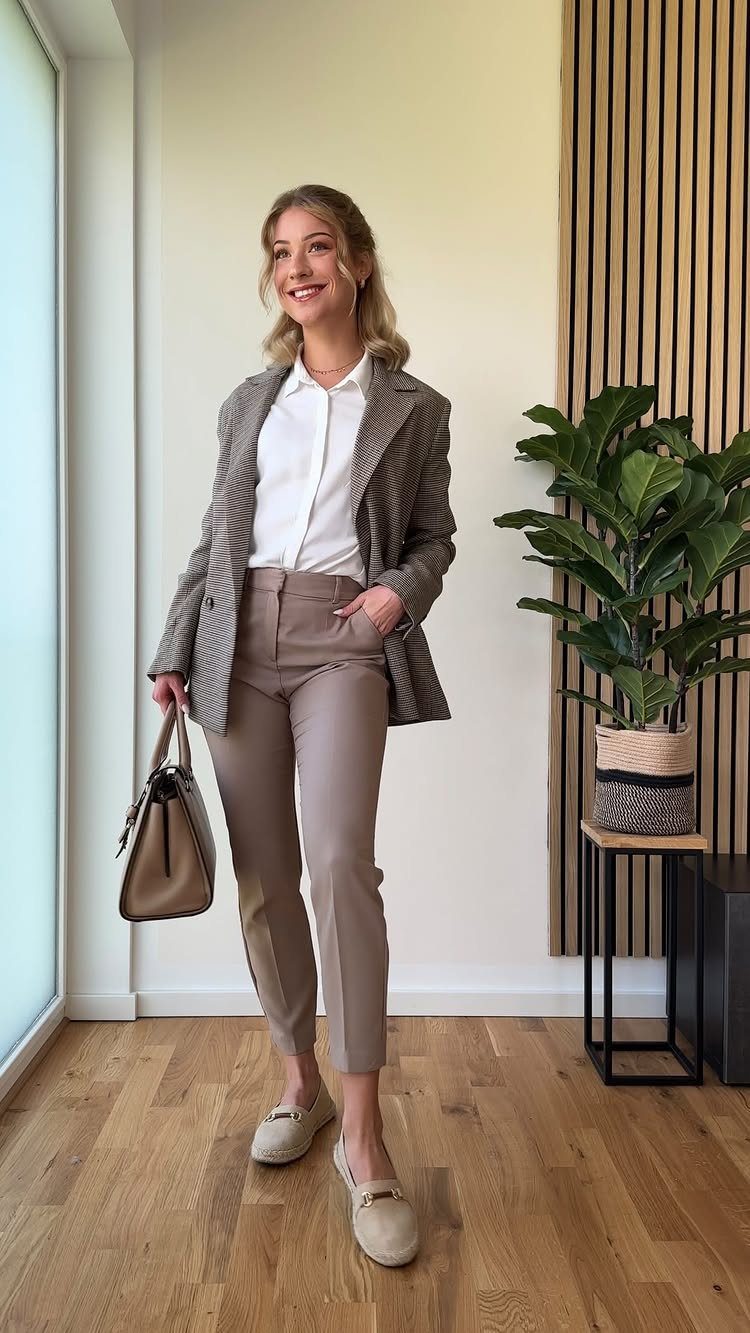 Woman in a brown patterned blazer and slim taupe trousers holding a brown handbag.