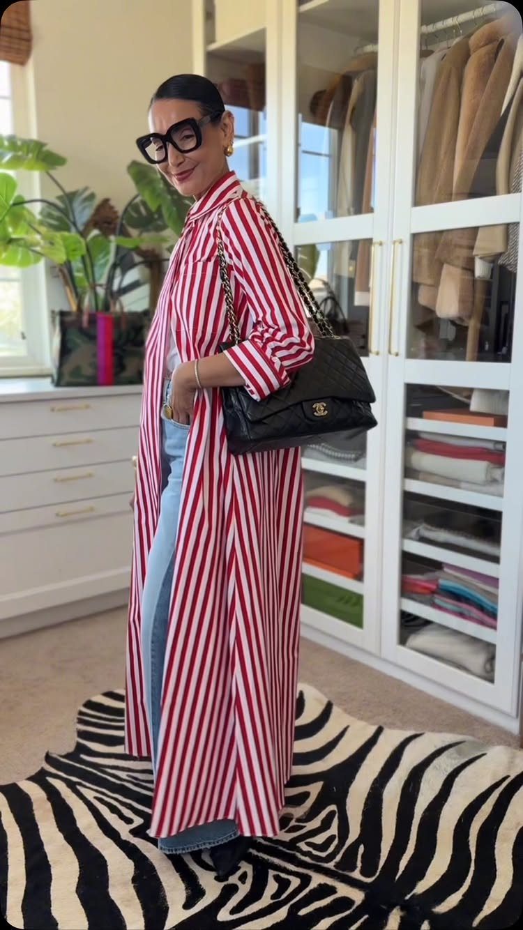 8 Fall Outfits for Women Over 50 to Wear Right Now 6 Woman in a long red and white striped shirt and blue jeans posing indoors.