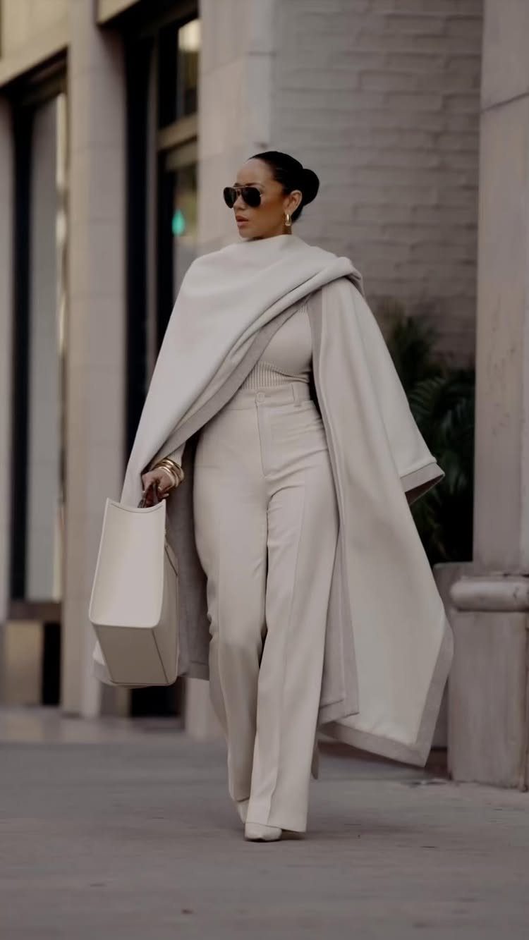 8 Fall Outfits for Women Over 50 to Wear Right Now 7 Mature woman in a cream jumpsuit and matching cape walking on a city street.
