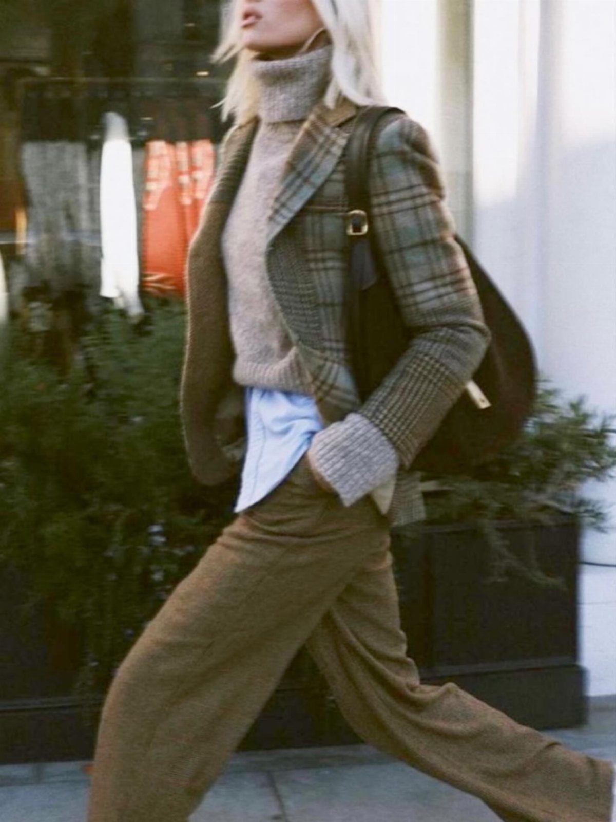 8 Fall Outfits for Women Over 50 to Wear Right Now 4 Woman wearing a brown plaid blazer, grey turtleneck, and wide-leg brown trousers walking outdoors.