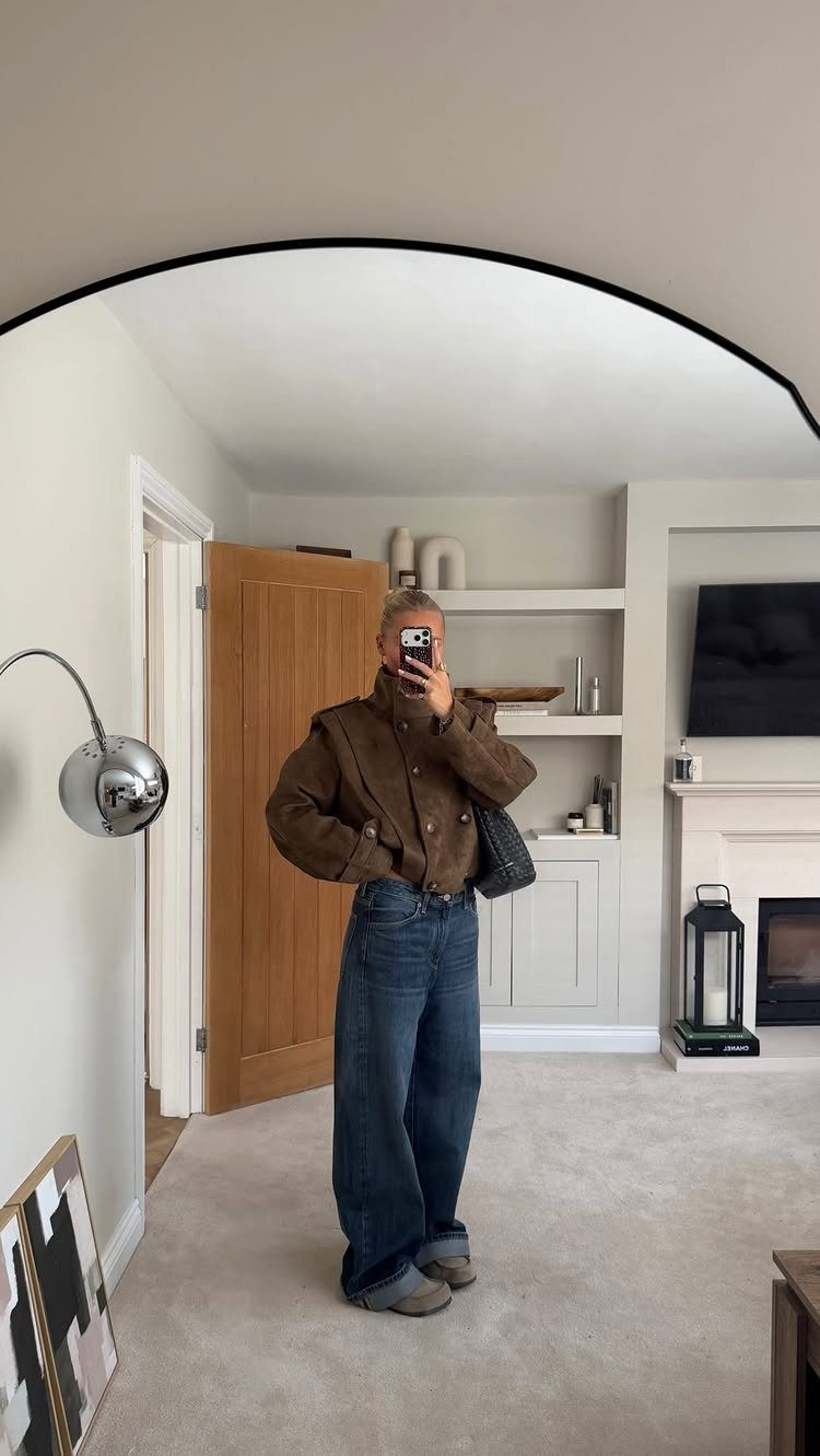 Fall Outfits for Women: 9 Ideas From Denim to Burgundy 3 Woman wearing a brown funnel-neck jacket and wide leg blue jeans in a room.