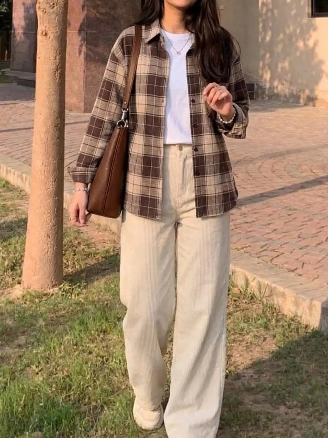 Gender Neutral Outfits: 9 Ideas Anyone Can Wear 5 Person wearing a brown plaid button-up shirt with cream wide-leg trousers and brown bag.
