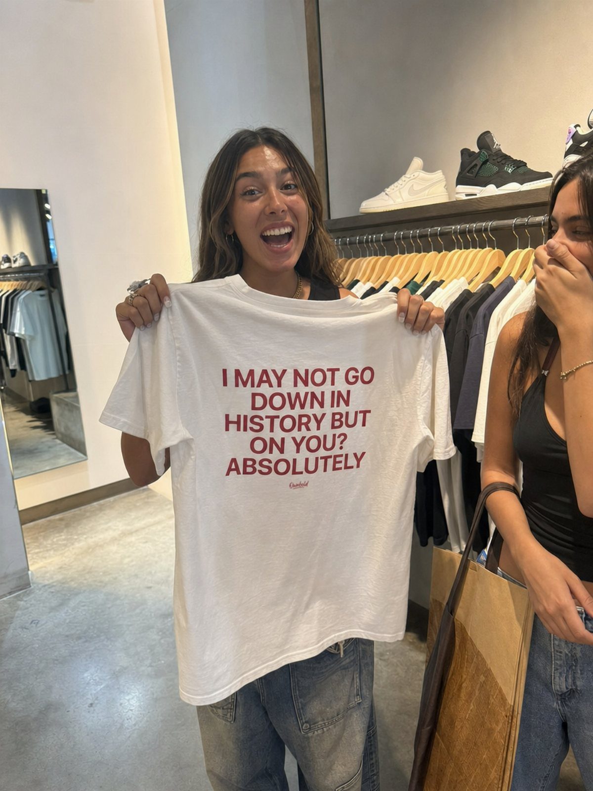 Gender Neutral Outfits: 9 Ideas Anyone Can Wear 1 Woman holding a white graphic t-shirt with red text in a clothing store.