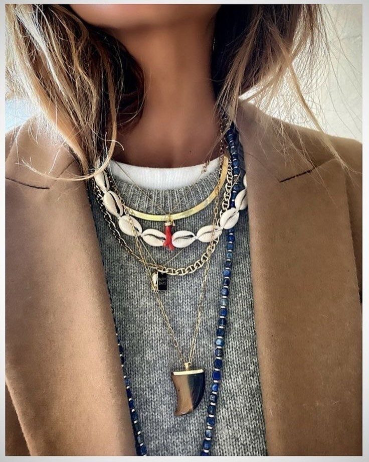 Gender Neutral Outfits: 9 Ideas Anyone Can Wear 9 Person wearing a tan blazer and grey sweater with layered shell and gold necklaces.