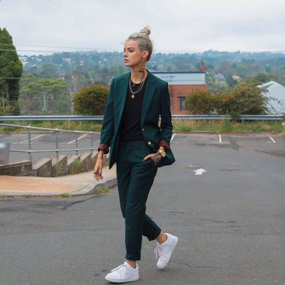 Gender Neutral Outfits: 9 Ideas Anyone Can Wear 8 Person wearing a dark green suit and white sneakers walking on a road.