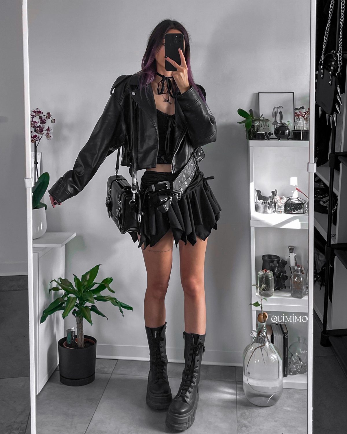 Person wearing a black leather jacket, pleated skirt with chains, and platform boots.