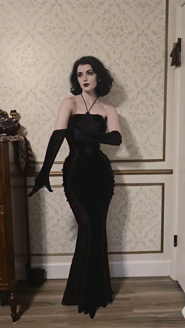 Woman in a long strapless black velvet corset gown and opera gloves.