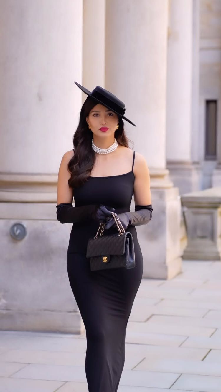 Great Gatsby Themed Outfits: 10 Ideas for Your Next Party 7 Woman in a black dress, hat, and pearls posing by white stone columns.