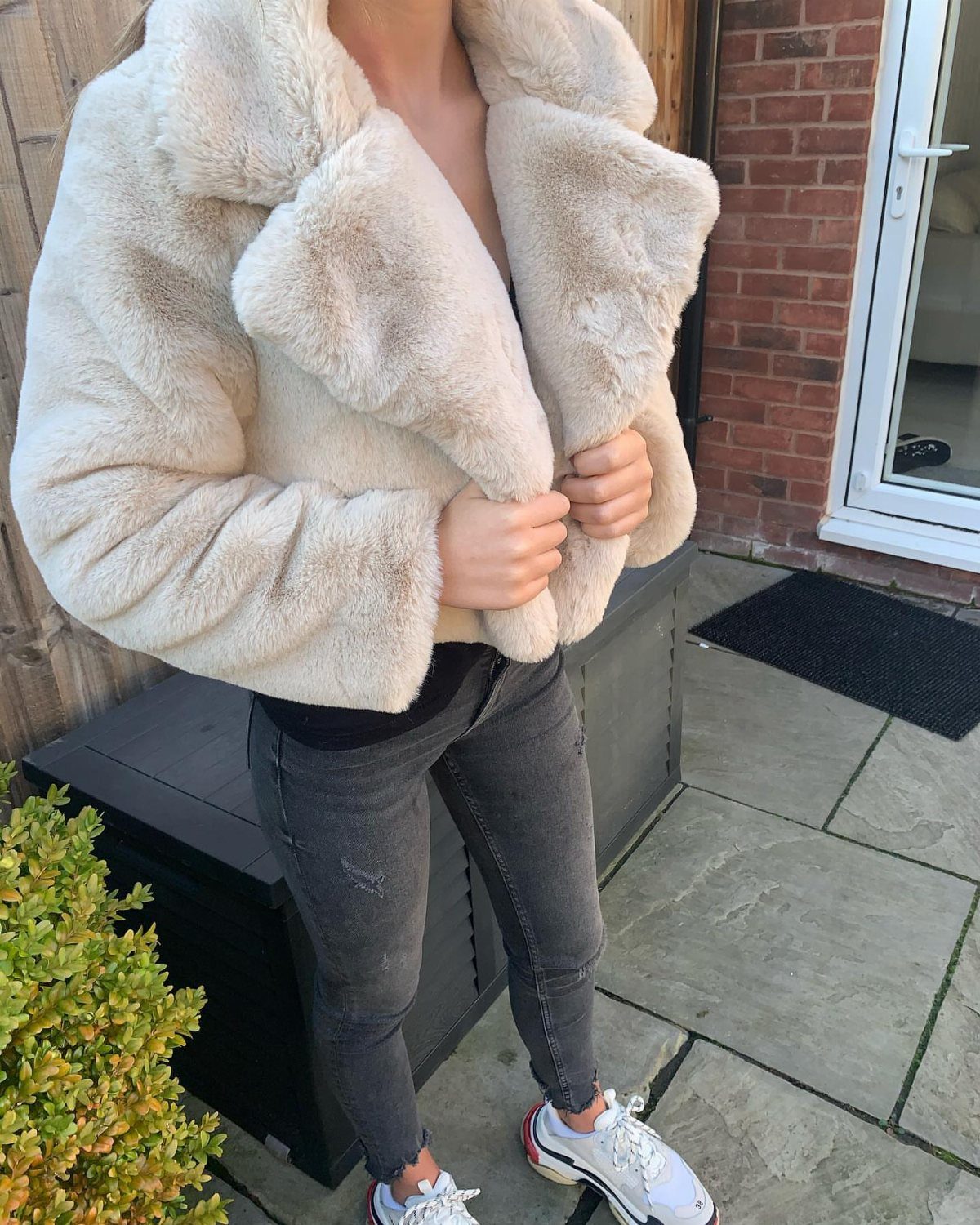 Person wearing a large cream faux fur jacket with grey jeans and white sneakers.