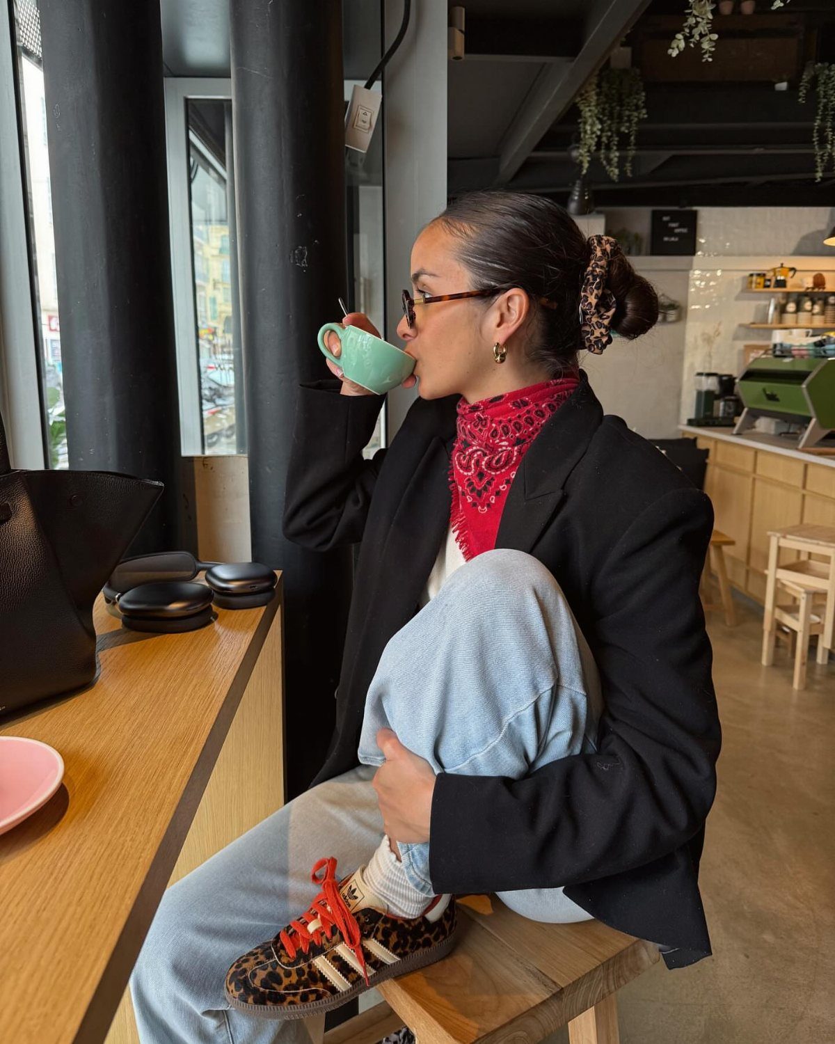 Woman in a black blazer and red scarf drinking coffee in a cafe.