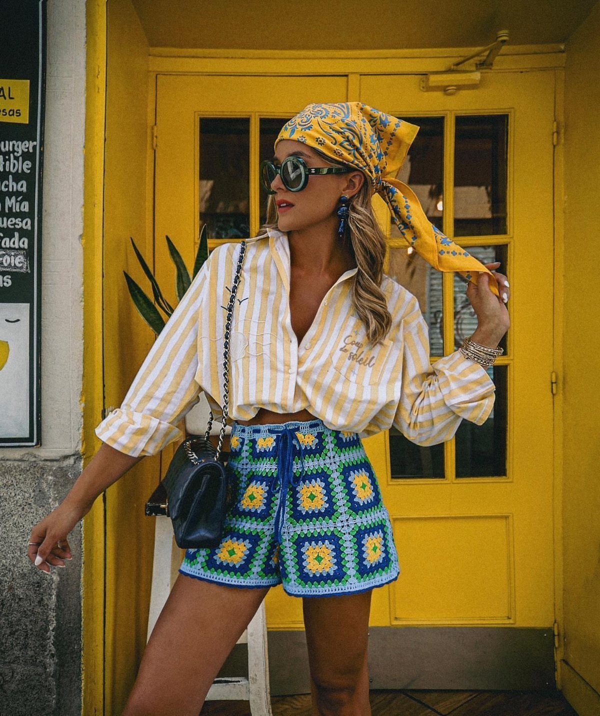 Woman in crochet high-waisted shorts and striped shirt posing by a yellow door.