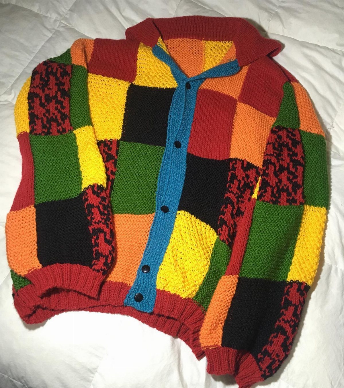 Colorful patchwork knit cardigan with red, yellow, green, and orange squares on white fabric.
