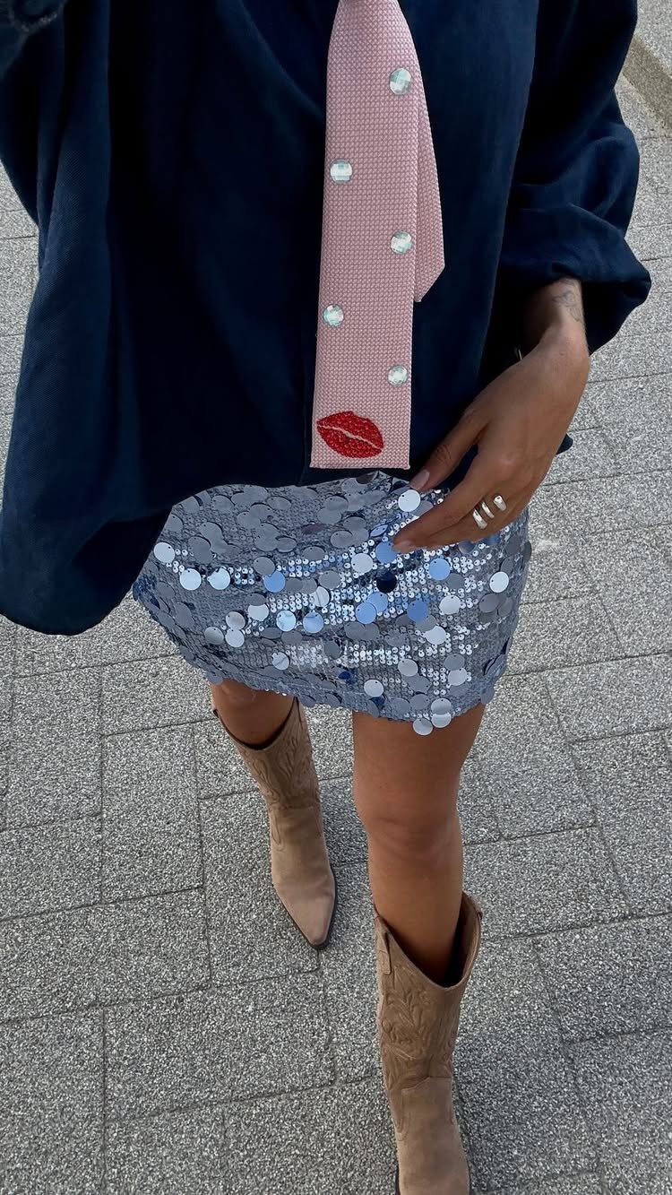 Person wearing a sequined skirt, pink tie, and tan boots for a concert outfit.