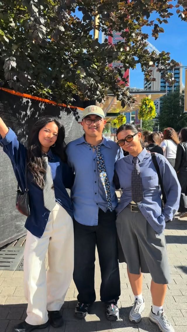 Three people wearing oversized shirts and ties standing outdoors under a tree