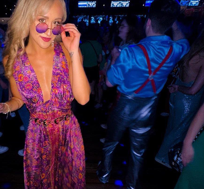 Woman in purple patterned dress and round sunglasses at a party event