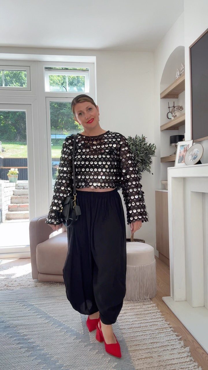 Woman wearing a black sequined crop top, black trousers, and red high heels.