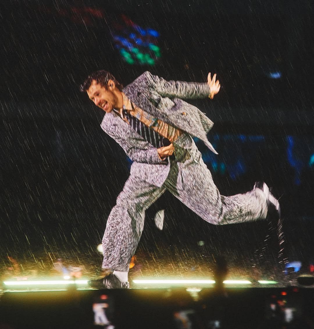 Harry Styles dancing in the rain wearing a grey patterned wide-leg suit.