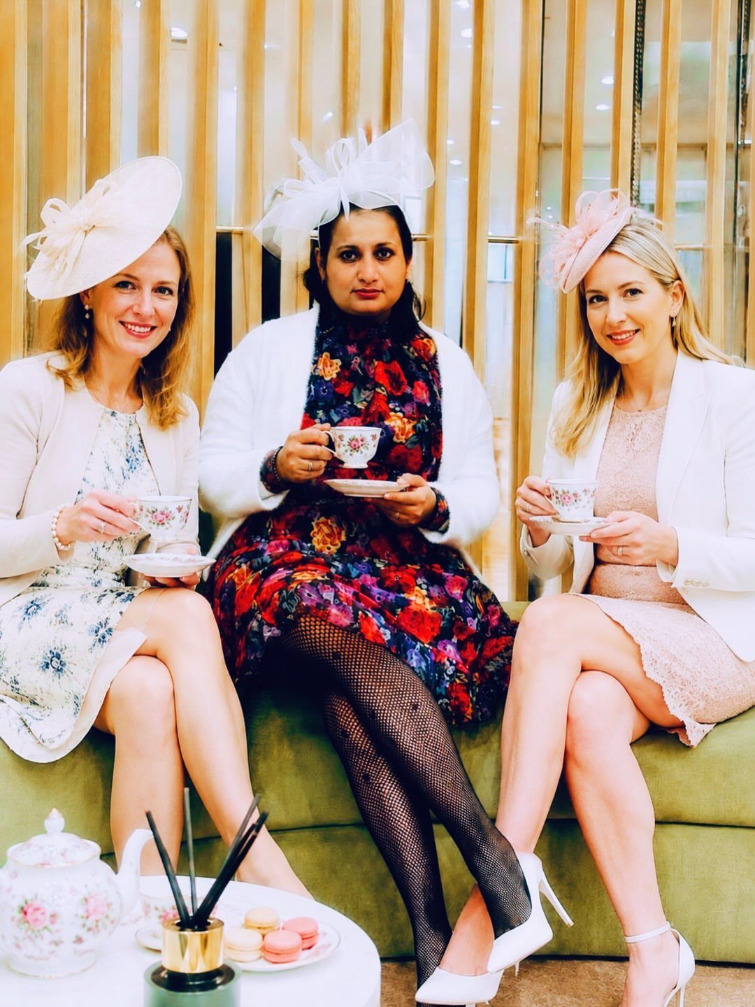 8 High Tea Outfits From Casual to Formal 6 Three women in elegant dresses and fascinator hats drinking tea at high tea.