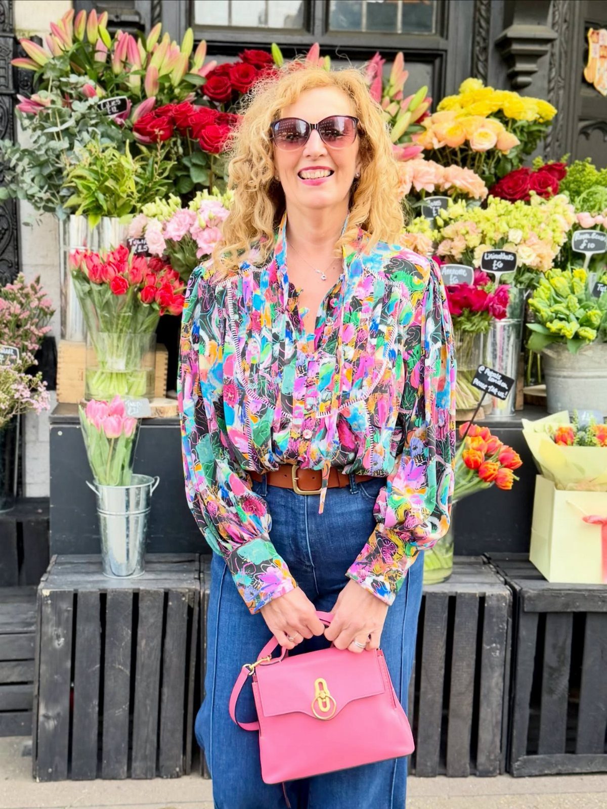 Hilary Banks Outfits: 12 Iconic Looks to Recreate Her Style 1 Woman wearing a vibrant multi-colored patterned blouse and blue jeans at a flower shop.