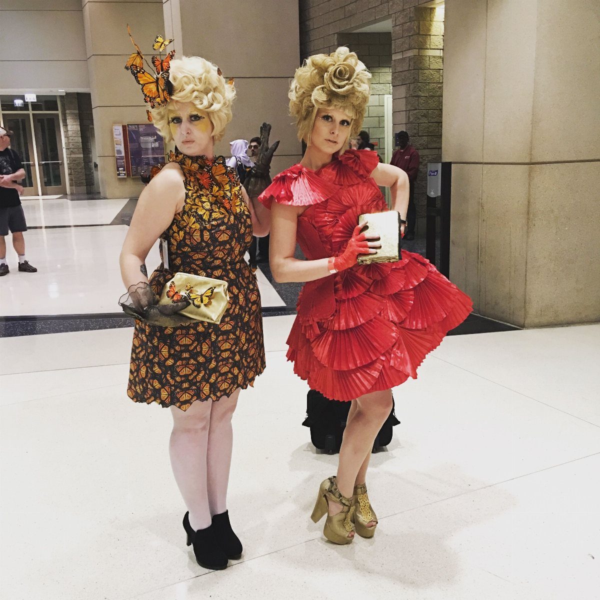 Hunger Games Outfits: 8 Iconic Looks from the Films 3 Two women in colorful, voluminous Capitol dresses and blonde wigs posing indoors.