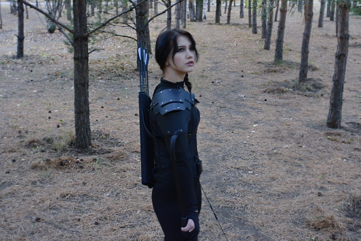Hunger Games Outfits: 8 Iconic Looks from the Films 2 Woman in black tactical hunting gear with shoulder armor and arrows in a forest