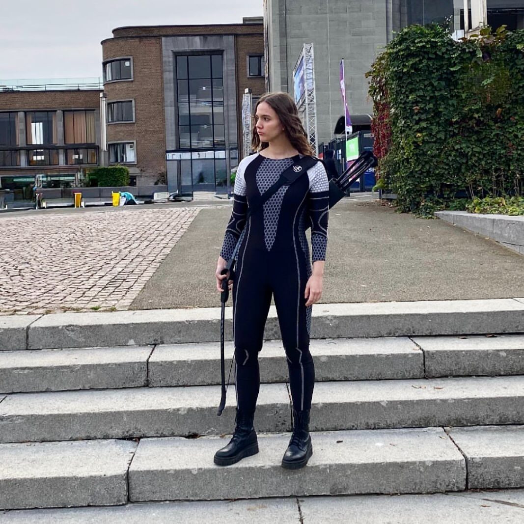 Hunger Games Outfits: 8 Iconic Looks from the Films 5 Woman in a black and grey futuristic bodysuit holding a bow and arrows.