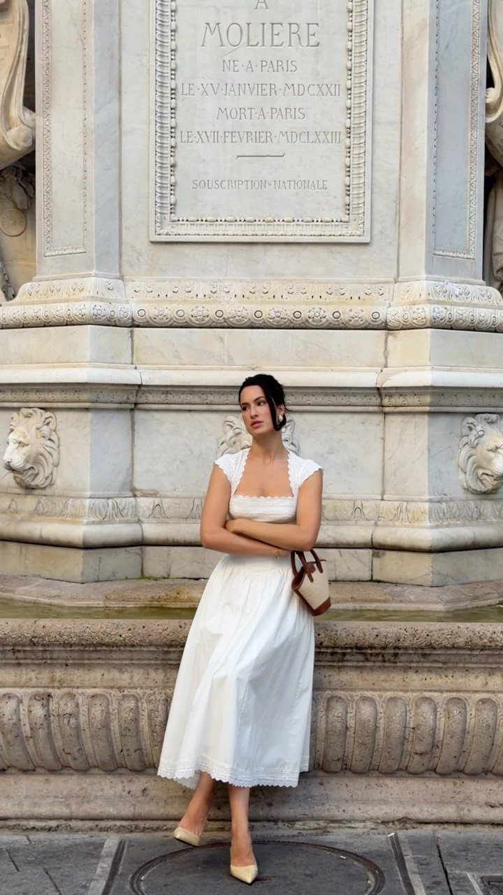 Woman in a white midi dress posing against a carved stone monument.