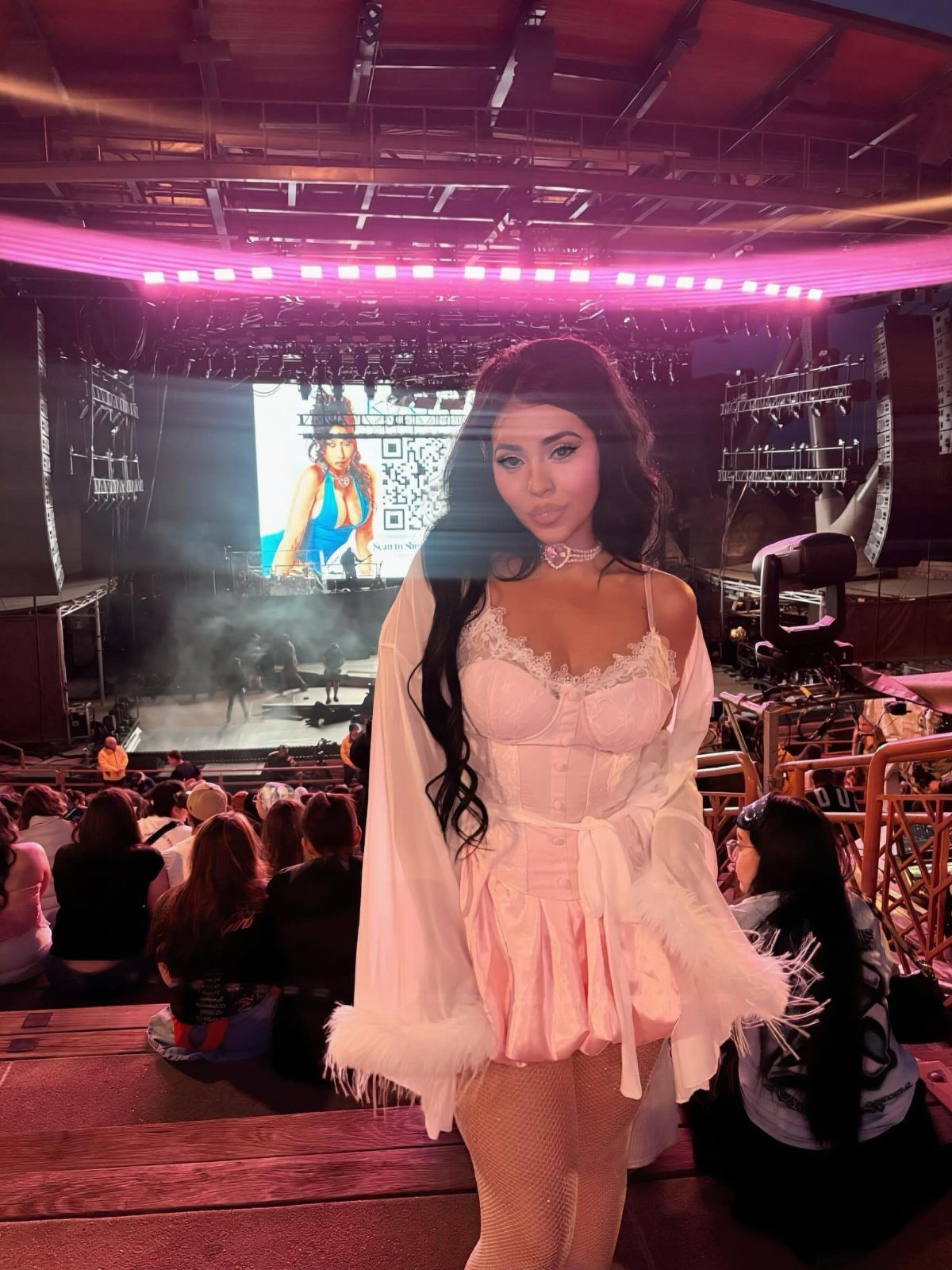 Kali Uchis Outfits: 12 Bold Looks for Retro Style 8 Woman in pink corset and white robe at an outdoor concert venue.