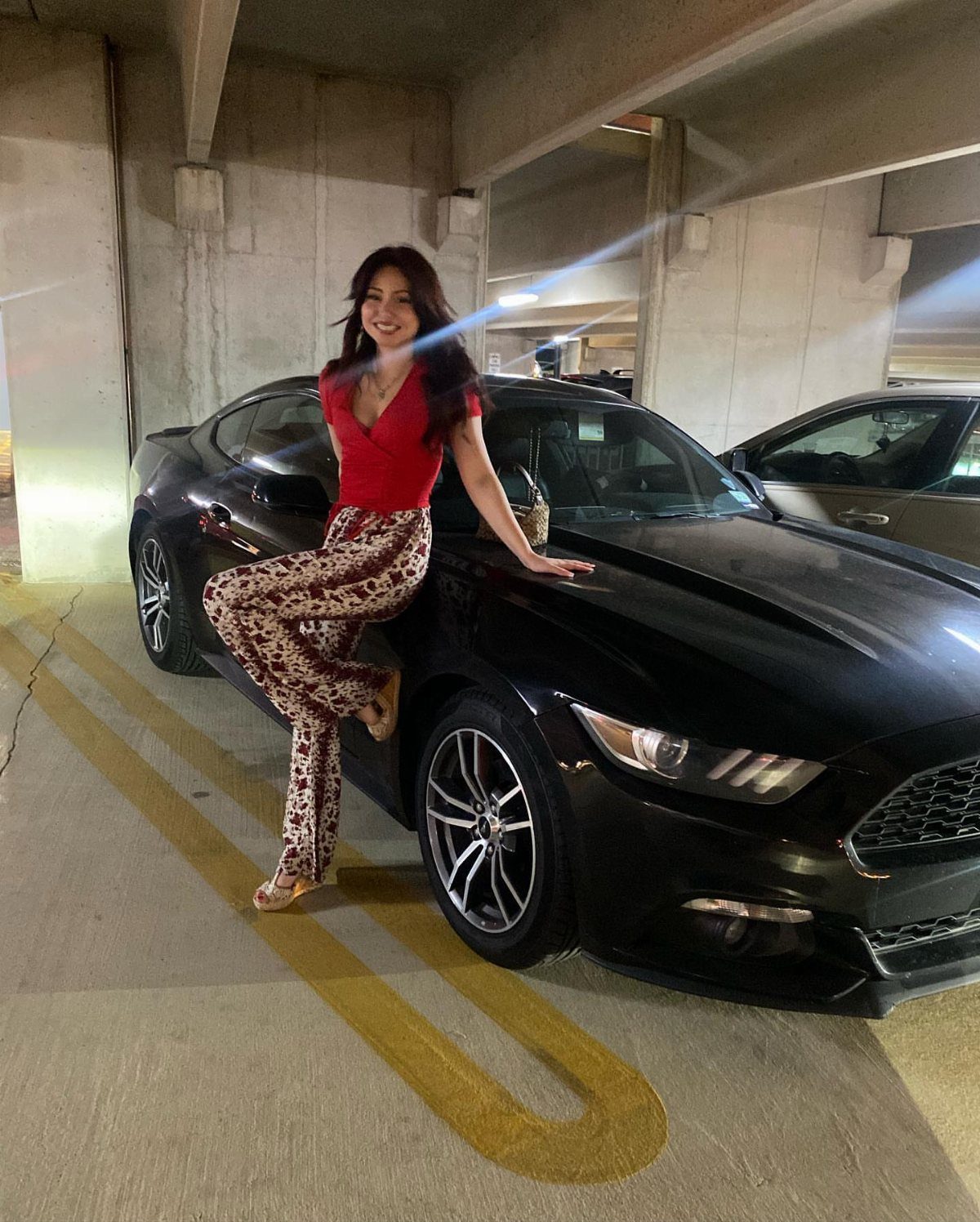 Kali Uchis Outfits: 12 Bold Looks for Retro Style 12 Woman in red top and floral high-waisted trousers posing by a black car.