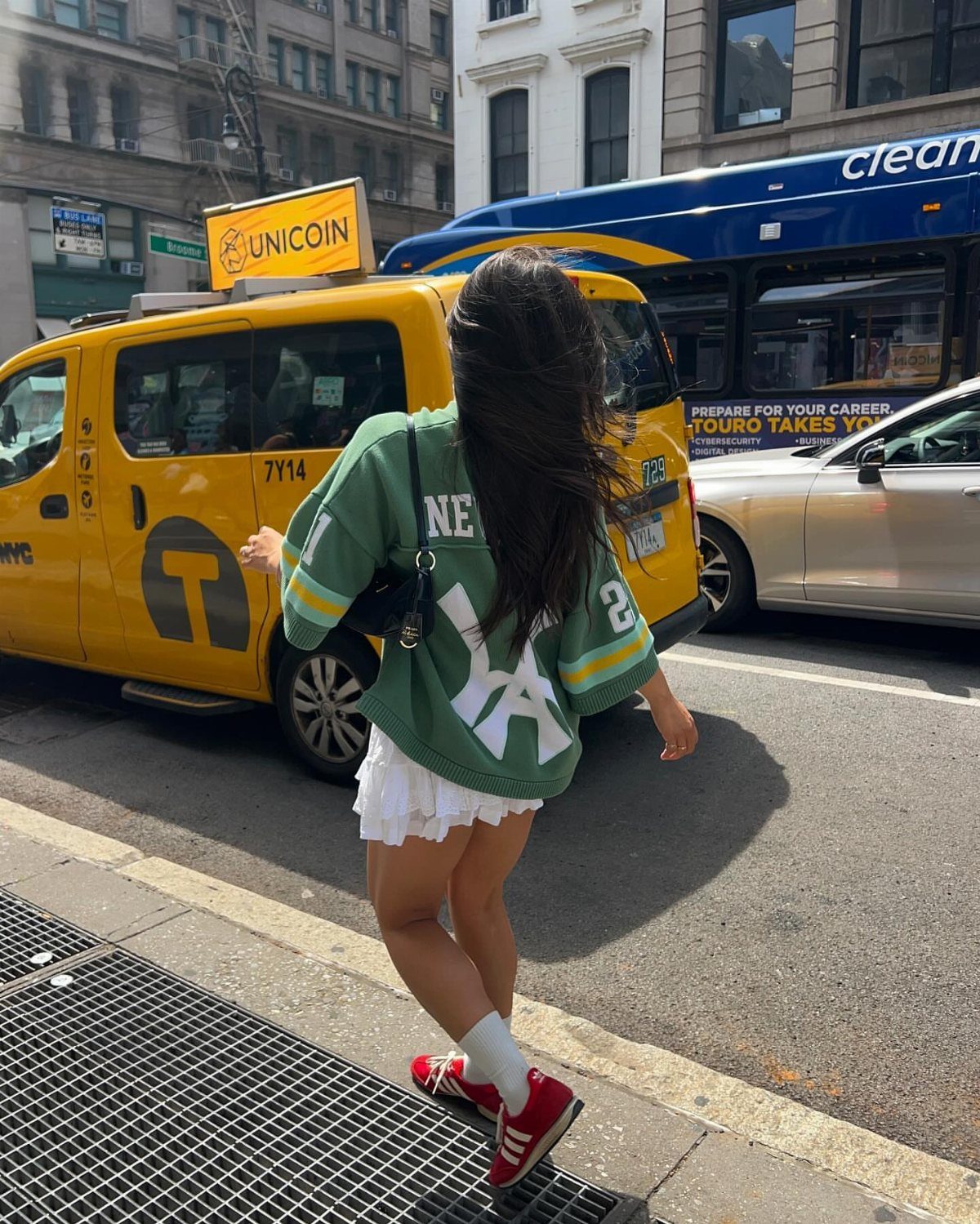 Kali Uchis Outfits: 12 Bold Looks for Retro Style 6 Woman in oversized green athletic jersey and white skirt standing on city street.